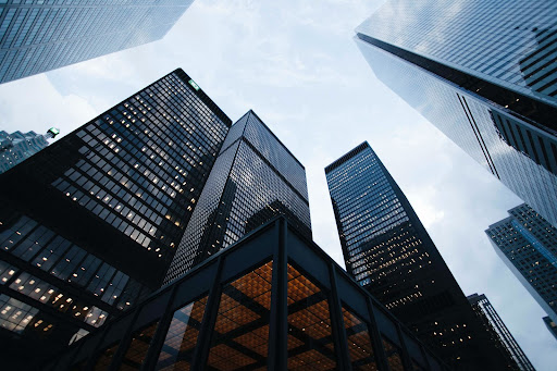 An upward shot of skyscrapers in a city, with a cloudy sky above.